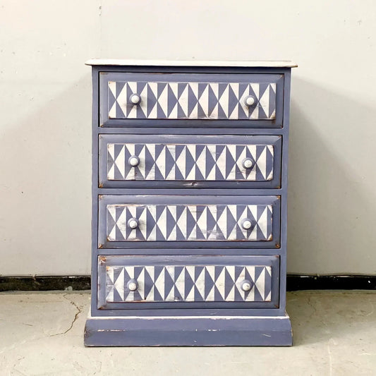 Vintage-style upcycled pine chest with four drawers, each adorned with a geometric white and purple triangle pattern, set against a neutral background. Rustic vibe.